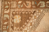 Distressed Oushak rug corner showing low pile with geometric hook and latch motifs in brown and seafoam.