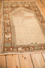 Angled view of a distressed Oushak prayer rug showing its worn texture and geometric border.