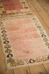Angled view of a distressed Anatolian mat highlighting its textured rose pile and ivory geometric border.