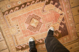 Vintage Kars rug with distressed pink and brown geometric motifs, viewed from above for scale.