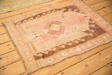 Angled view of a distressed Kars rug with a geometric prayer design in faded pinks and coffee brown.
