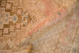 A fold reveals the distressed texture and low pile of an Oushak rug in bronze, rose, and blue hues.