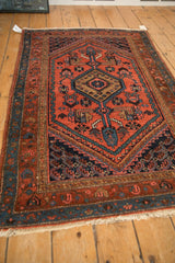 Angled view of a vintage Kurdish Hamadan rug showing its madder red field and geometric medallion design.