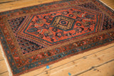 Angled view of a vintage Kurdish Hamadan rug with a red field and a serrated hexagonal medallion.
