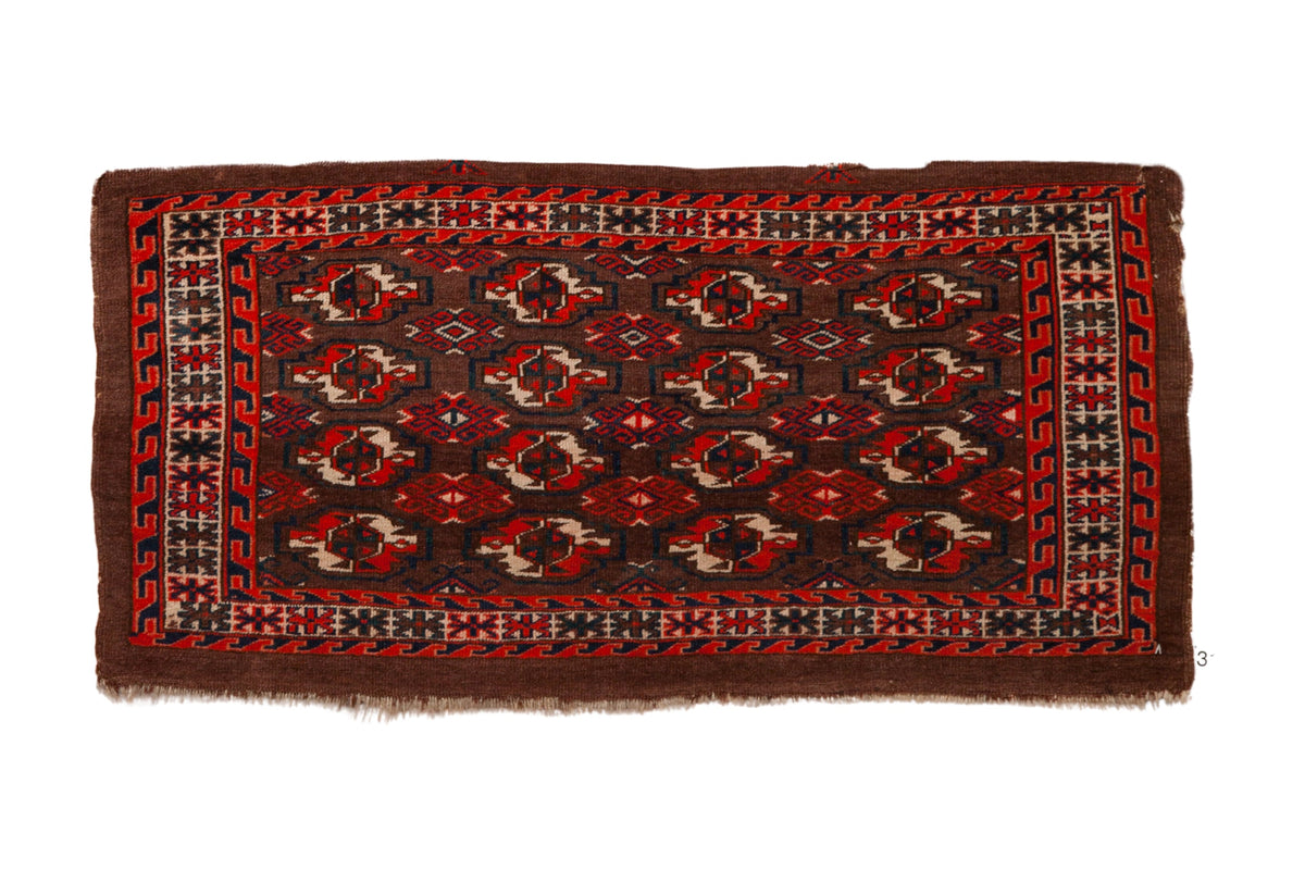 Antique Turkmen rug with repeating geometric guls in tomato red, navy blue, and ivory on a coffee brown field.
