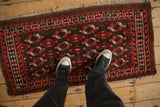 A person's view of a small antique Turkmen rug showing scale against its geometric pattern.