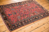 Angled view of an antique Lilihan rug with a raspberry red field and complex, dark floral border.