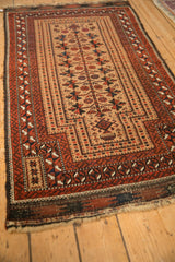 Antique Persian Belouch rug shown at an angle, highlighting its geometric serpent borders and sand-colored field.