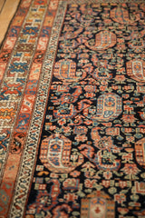 Angled view of an antique Hamadan rug's colorful crab border and navy boteh-filled field.