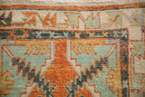 Detailed view of the worn hand-knotted pile and geometric border in burnt orange and jade green.