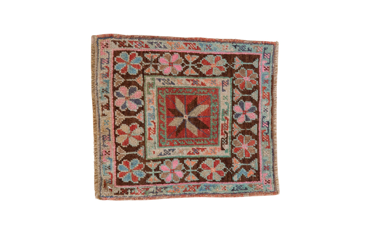 Vintage distressed Oushak square mat with a central pinwheel floral design and colorful wave motif border.