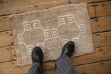 Distressed Oushak rug showing muted tones and white interlocking geometric pattern.