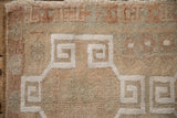 Distressed Oushak rug pile, white scrolled contour on muted beige field.