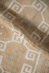 Textured pile of distressed Oushak rug, revealing white geometric border motif.