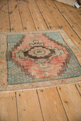 Corner of distressed Oushak rug with serrated melon and denim blue geometric patterns, visible fringe.