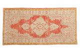 A distressed vintage Oushak rug with a faded cherry red medallion, ivory ground, and saffron yellow details.