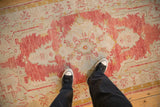 Overhead view of the distressed, low-pile texture on a vintage Oushak rug's faded red medallion.