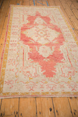 Angled perspective of a vintage Oushak rug with a faded red medallion and soft, worn texture.