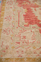 Angled close-up of the distressed Oushak rug showing low, worn pile and faded cherry red motifs.