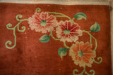 Detail of an Art Deco rug's rosette blossoms and curved jade green vines on a copper field.