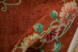 Rolled corner of a vintage Art Deco rug showing the plush copper pile and a large floral rosette.