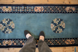 Person's view of a vintage Peking runner showing the floral medallion, border, and sky blue pile.