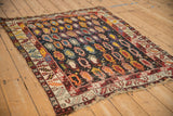 Antique Caucasian rug with dense boteh motifs and tattered borders, seen from an angled perspective.