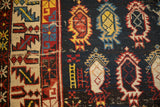 Flame-like boteh motifs and tribal border on an antique Caucasian rug with visible wear to the foundation.