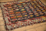 Full angled view of an antique Caucasian rug highlighting its dense boteh field and tattered edges.