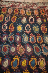 Antique Caucasian rug's pile showing worn texture and rows of colorful, flame-like boteh motifs.