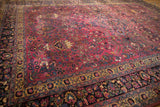 Angled view across the vintage Meshed carpet's pile, showing the detailed floral borders and purple field.