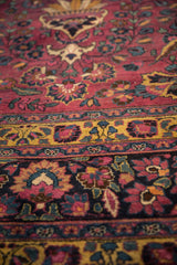 Close-up of a vintage Meshed carpet showing a saffron border and scrolling vines on a purple field.