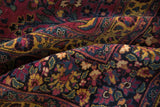 Detailed view of a folded vintage Meshed rug with rich aubergine, navy, and saffron floral patterns.