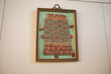 Lower right corner of framed, hand-embroidered textile pouch with geometric patterns and red pom-pom.