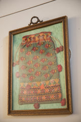 Ornate framed antique embroidered pouch with silk luster and warm-toned patterns.