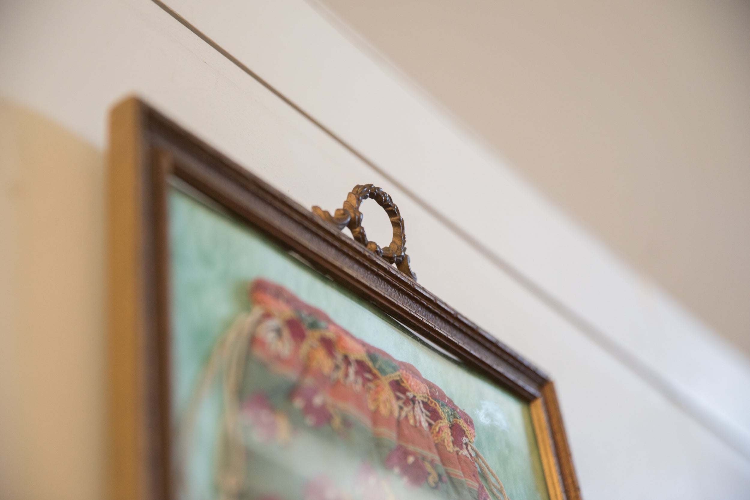 Ornate scrolling metal hanging loop and dark frame of the antique textile pouch.