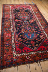Close-up of a vintage Hamadan rug corner, showing rust field with geometric elements and navy turtle samovar border.