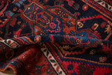 Curled pile of a vintage Kurdish Hamadan rug, highlighting navy, red, and rust tendril motifs.
