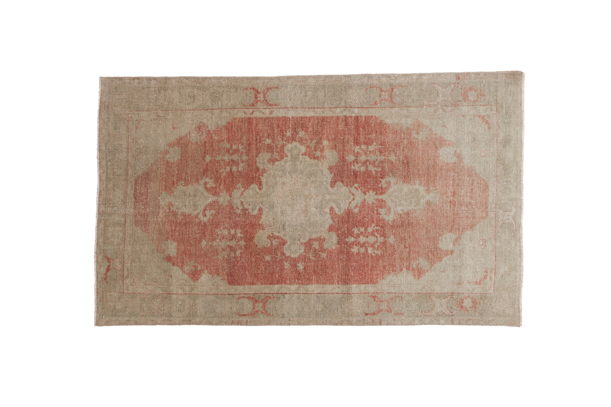 Vintage Oushak rug with a distressed, faded red turtle medallion on a sandy, abrashed ground.
