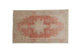 Vintage Oushak rug with a distressed, faded red turtle medallion on a sandy, abrashed ground.
