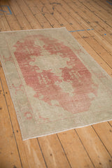 An angled view of the distressed vintage Oushak rug, showing its faded ruby-red medallion and low-pile texture.