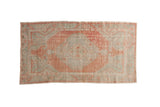 Distressed vintage Oushak rug runner with a faded diamond medallion in pale seafoam and ruby grapefruit hues.