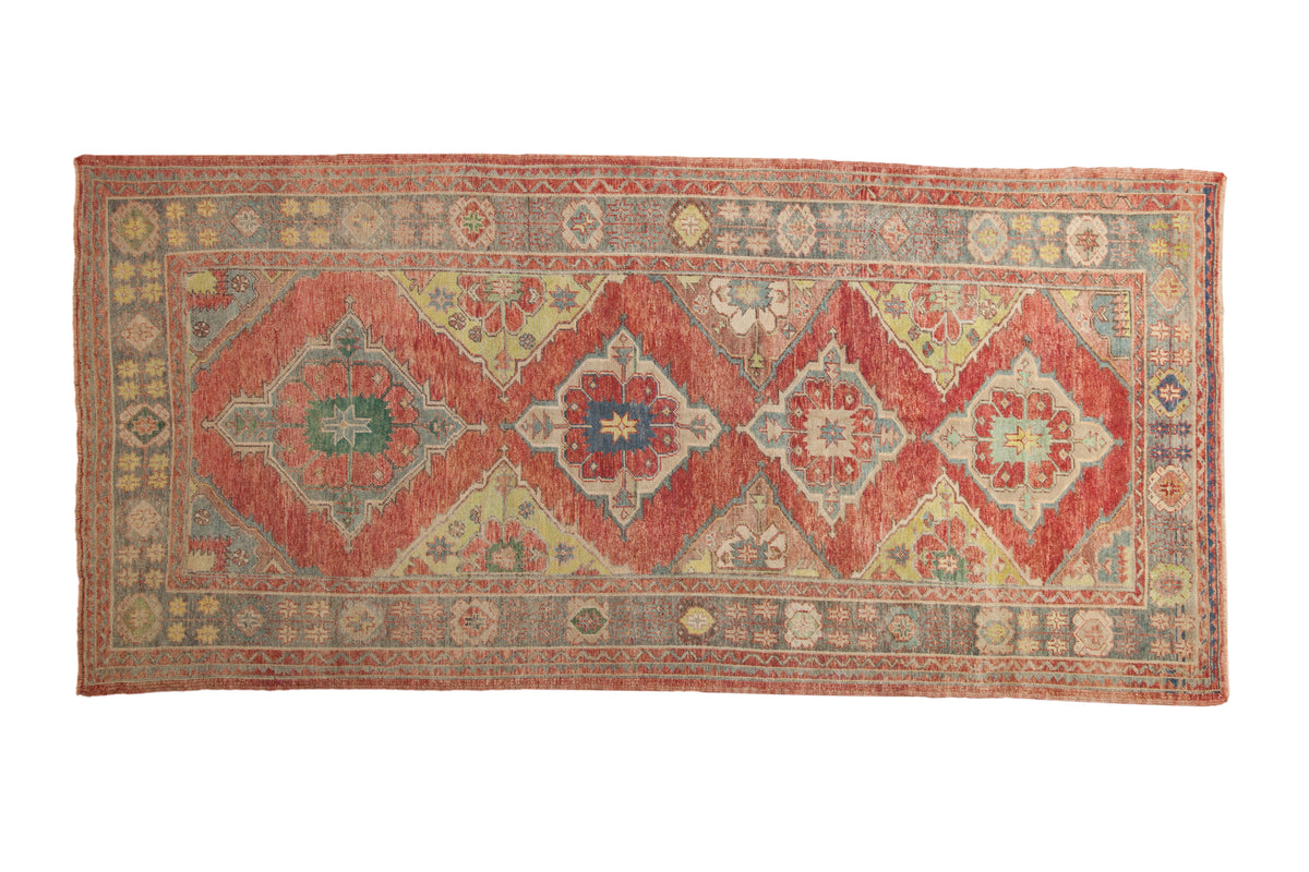 Distressed Oushak runner with a column of geometric diamond medallions in ruby red, green, and saffron yellow.