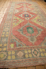 Angled perspective of a vintage Oushak runner's diamond medallions in faded ruby red and green.