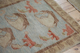 Powder blue field of Oushak rug with tan, cinnabar floral motifs, and spiral border.