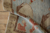Rolled modern Oushak rug with wool texture, spiral border, and blue, red, ivory patterns.