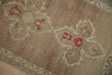 Distressed Oushak rug showing worn abrashed ground and red floral blossoms.