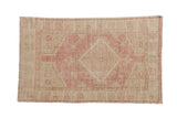Distressed vintage Oushak rug with dusty pink diamond medallion, ivory field, and soft abrashes.