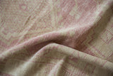 Soft abrashes across the hand-knotted Oushak rug's dusty pink and ivory pile.