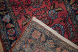 Vintage Mehreban rug's folded corner, showing hand-knotted back and raspberry, navy floral pile.